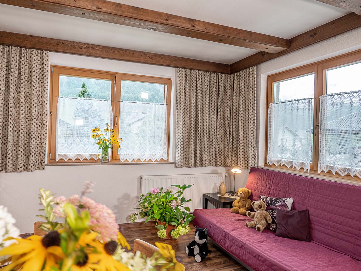 Eine lila bezogene Couch mit vielen Blumenvasen und 3 Teddybären auf der Couch
